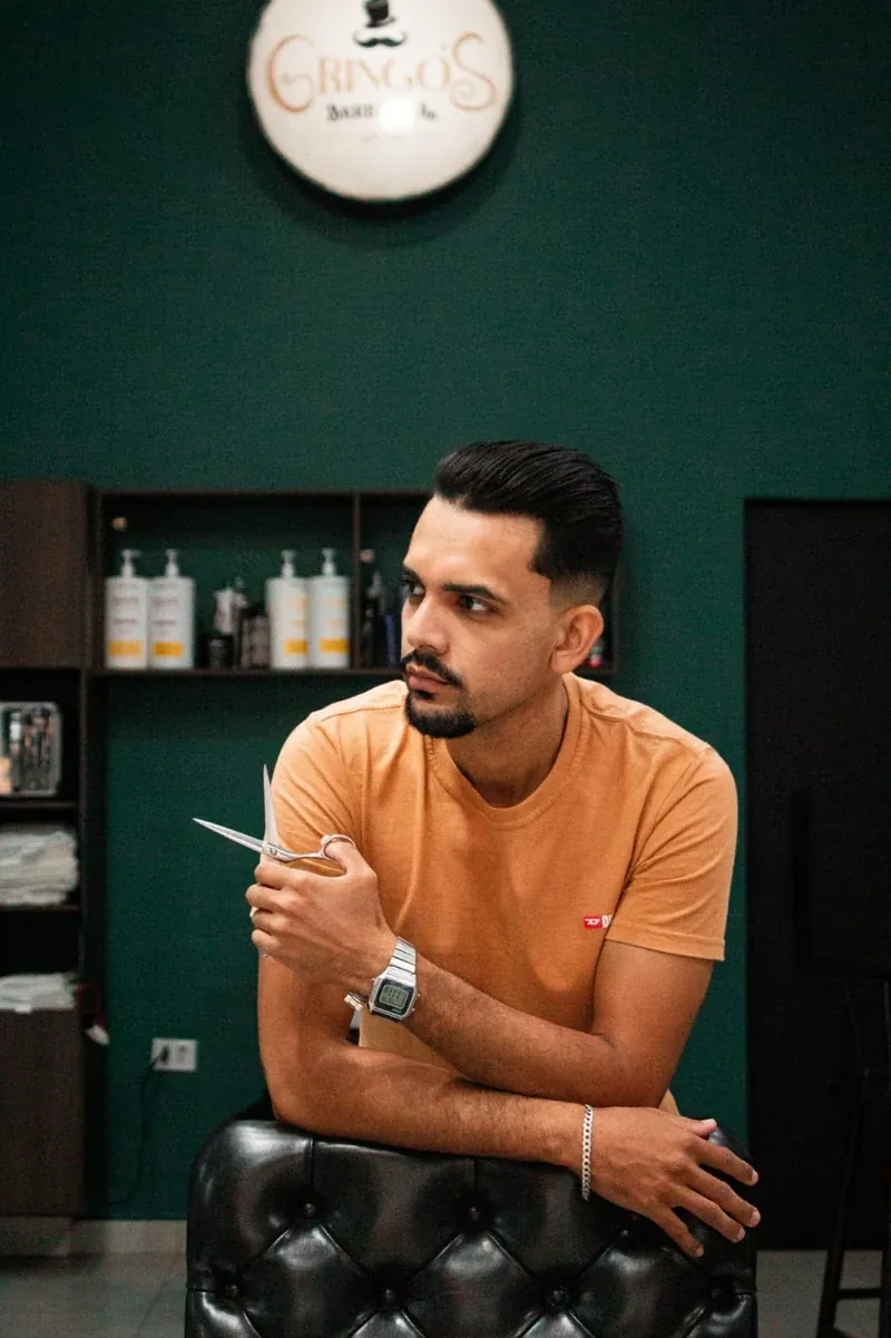 Barbeiro da Gringo's Barbearia com a tesoura na mão, no salão de paredes verdes